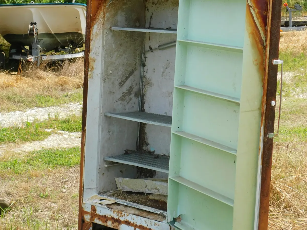 An old rusty refrigerator with its door open, sitting outside in a grassy lot.