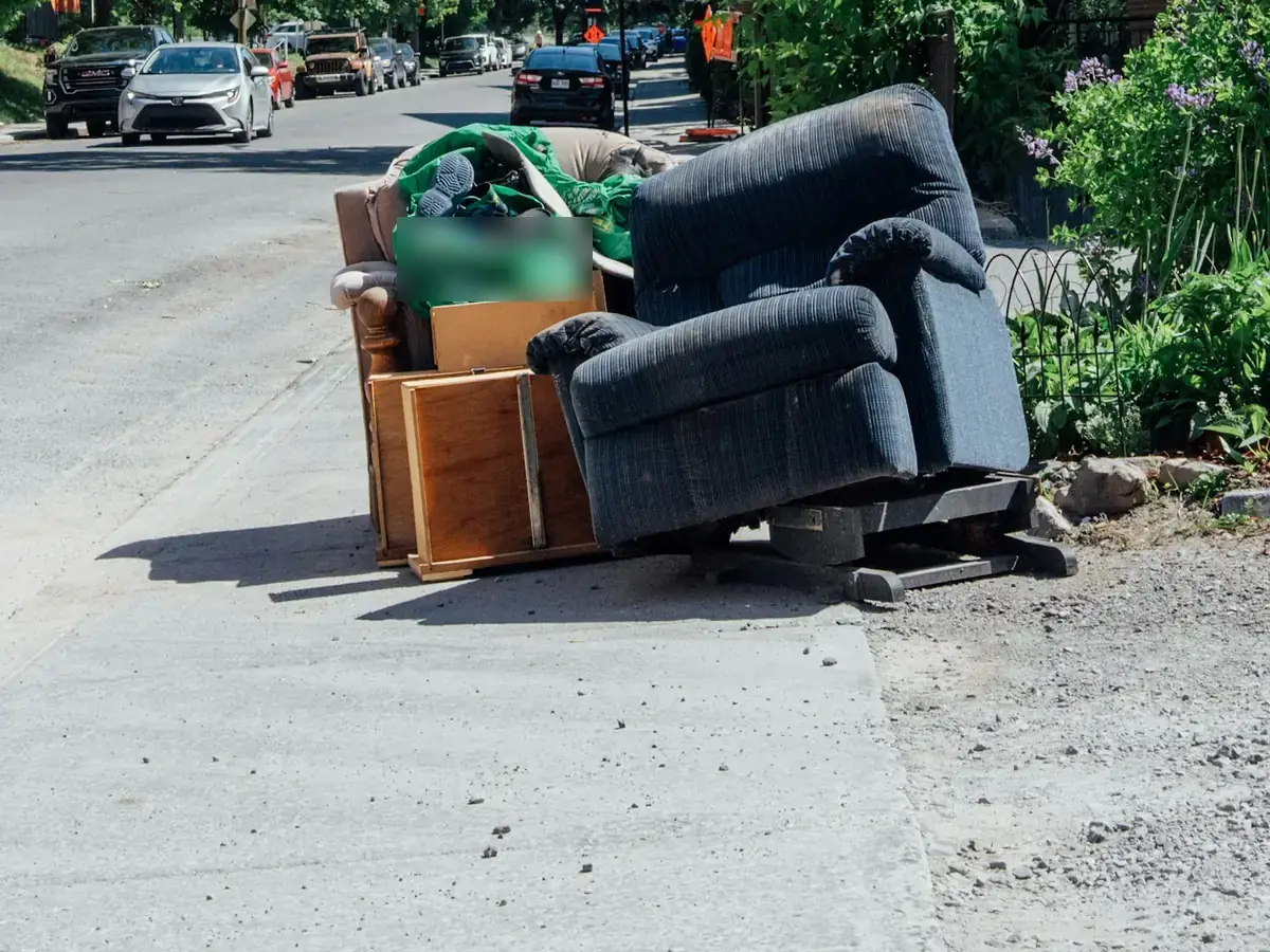 A blue recliner, an armchair and wooden furniture pieces piled at the curb.