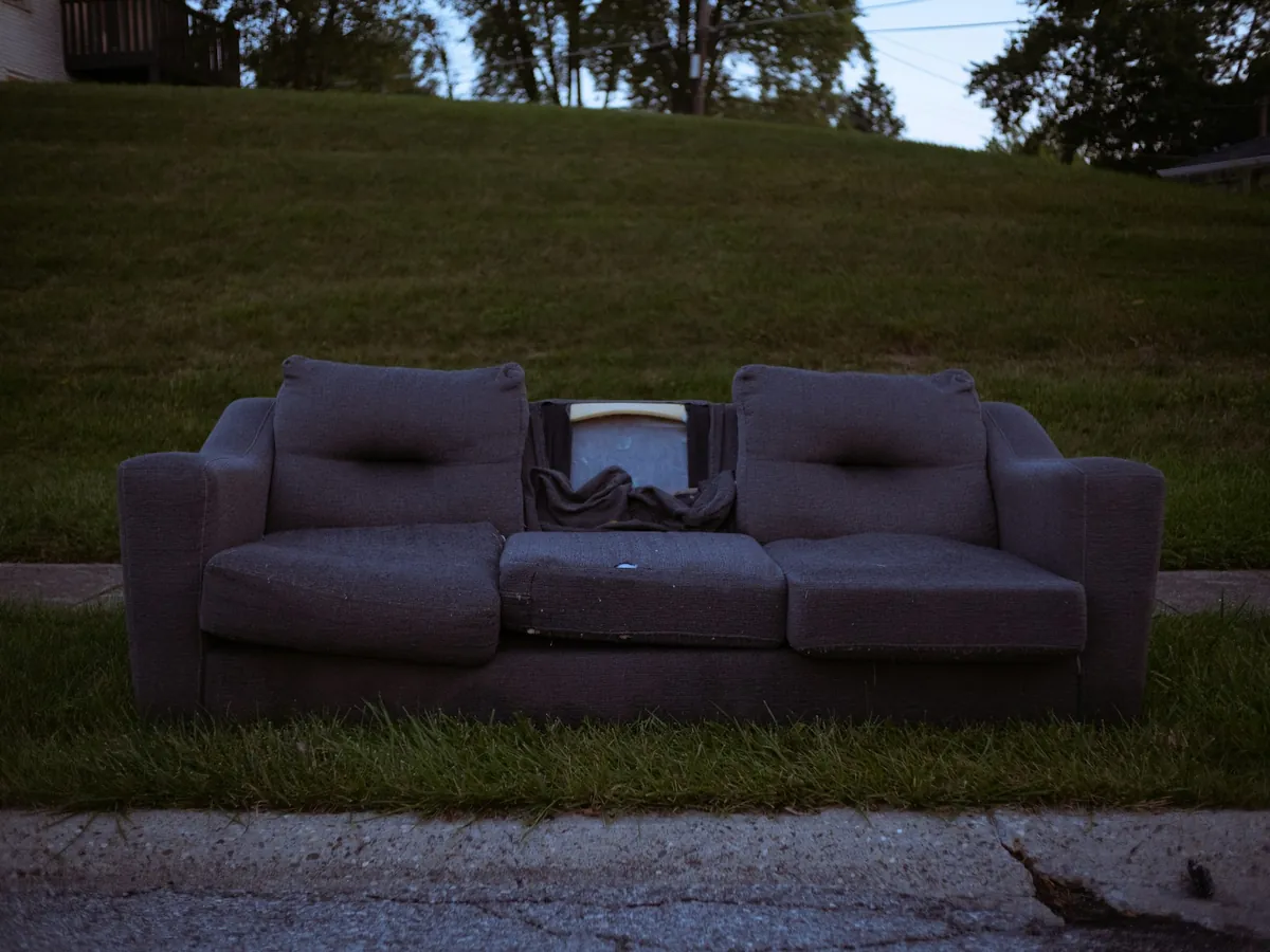 An old gray couch left on a grassy curb, waiting for pickup.