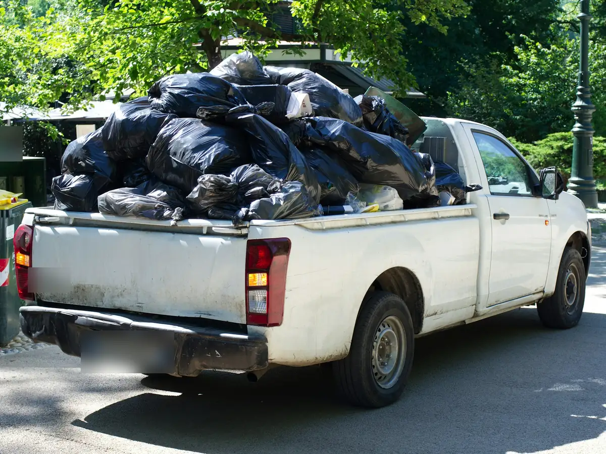 A white pickup truck with its bed piled high with black trash bags.